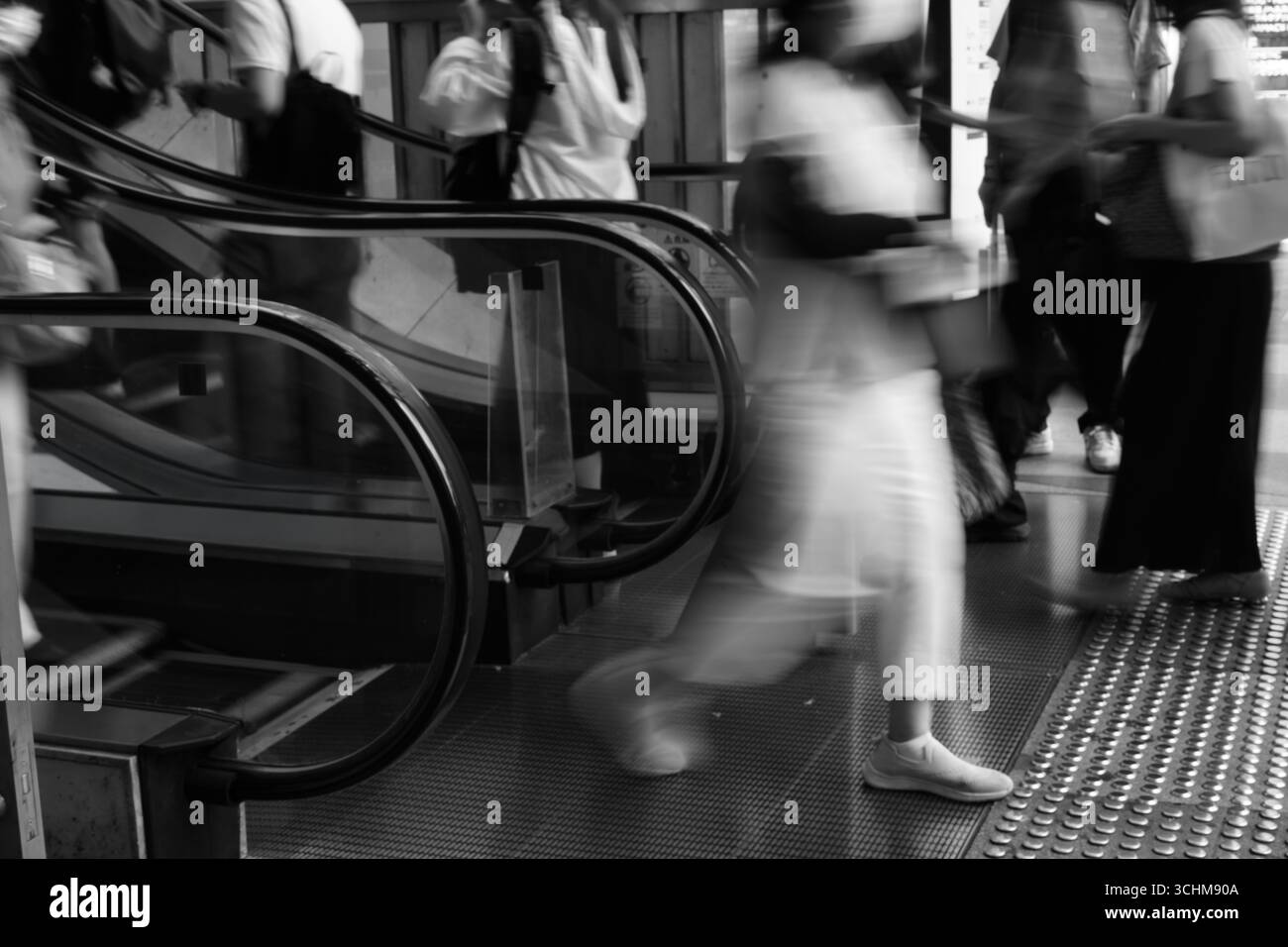 Bewegungsunscharfe Frau verlässt die Rolltreppe in einer geschäftigen Stadtszene und fängt das flüchtige Tempo des urbanen Lebens ein. Stockfoto