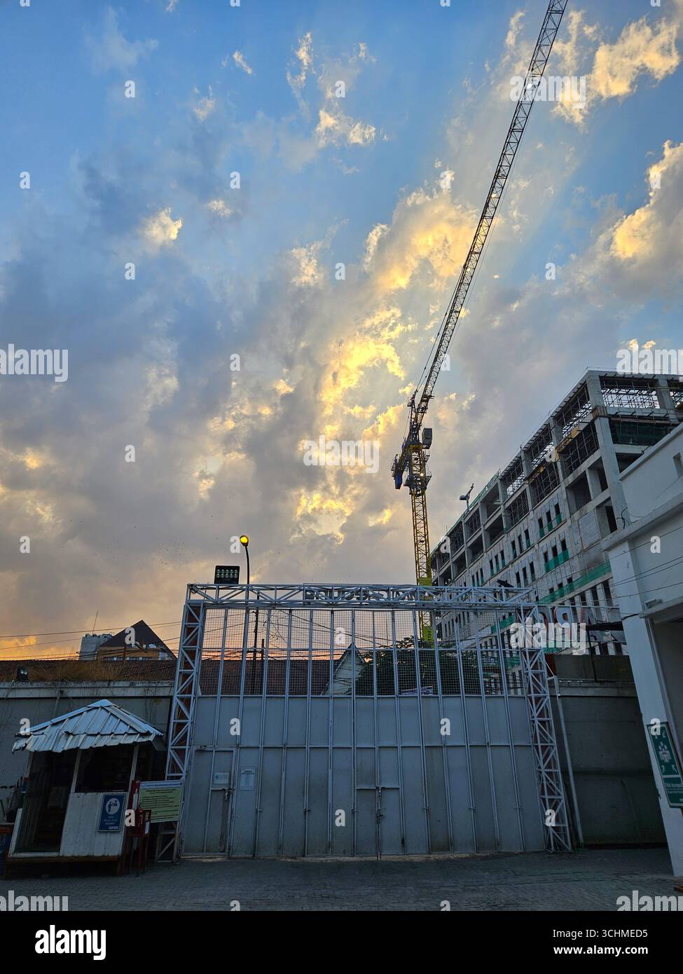 Baustelle mit Turmkran und unvollendetem Gebäude unter dramatischem Abendhimmel. Bandung, Indonesien - 1. Oktober 2023 - Smartphone-aufgenommenes Stockfoto