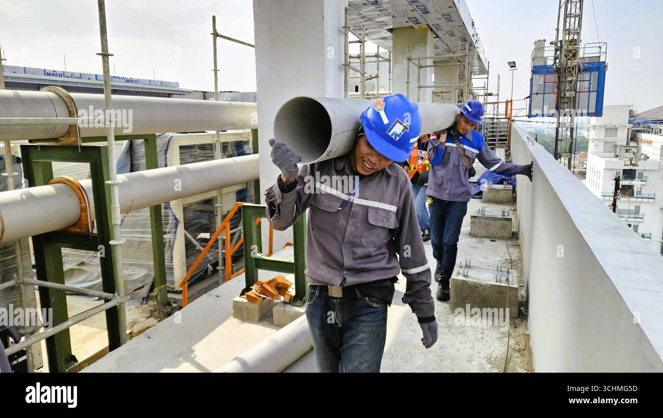 Bauarbeiter mit schwerem Rohr auf der Industriebau mit Schutzhelm und Uniform. Bandung, Indonesien - 30. November 2023 - Smartphone-aufgenommenes Stockfoto