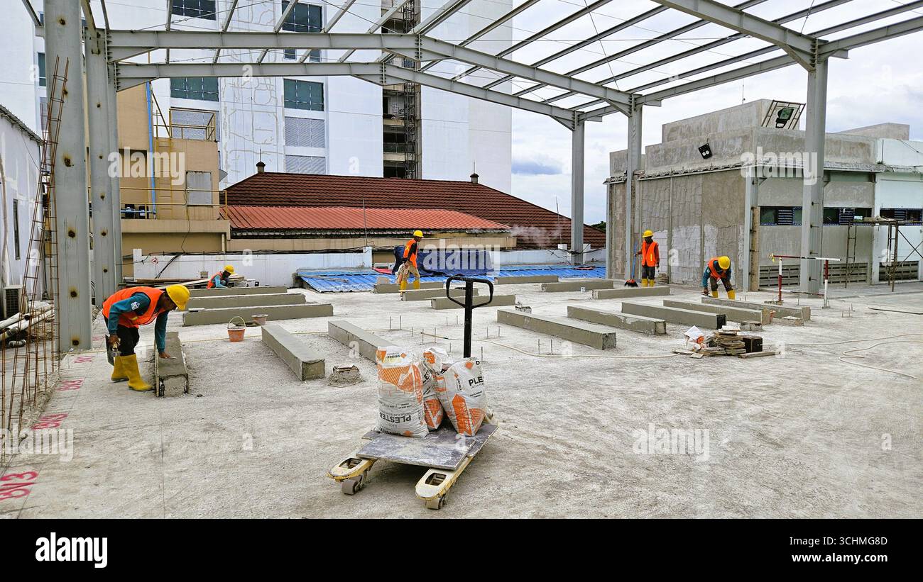 Gruppe von Bauarbeitern, die eine Struktur auf dem Dach mit Stahlrahmen und Betonboden montieren. Bandung, Indonesien - 17. Januar 2024 - Smartphone-aufgenommenes Stockfoto