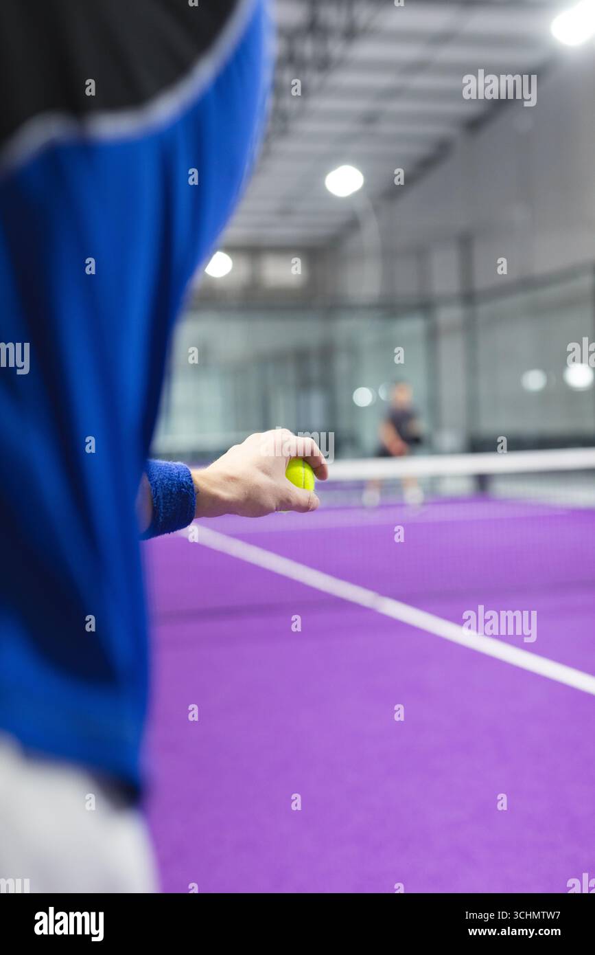 Männliche Gegner stehen auf einem violetten Platz in der Sporthalle, einer serviert Tennisball, Kopierraum Stockfoto