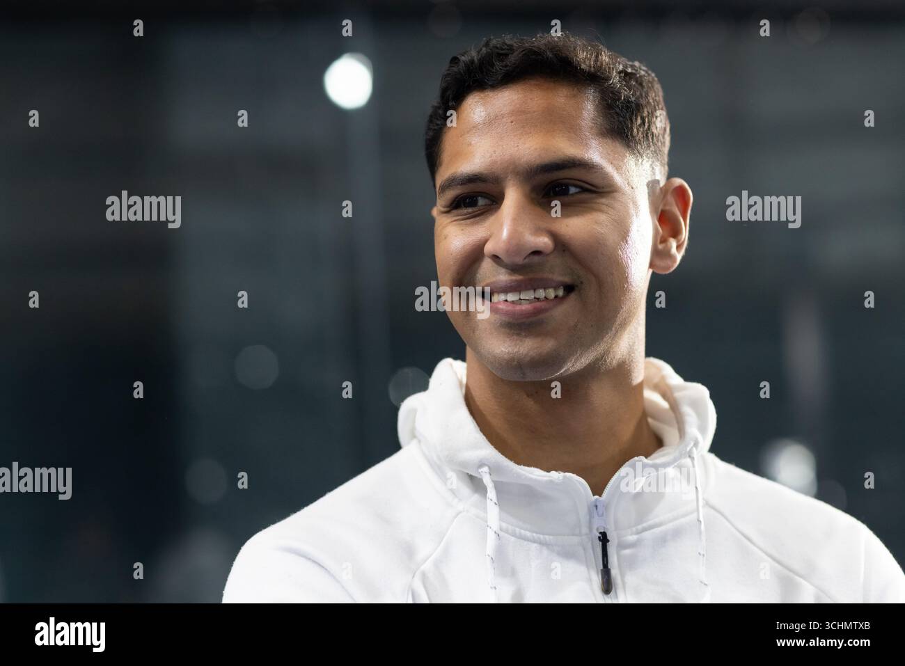 Erwachsener indischer Mann, der im Fitnessstudio vor getönten Glasplatten in weißem Sport-Hoodie steht Stockfoto