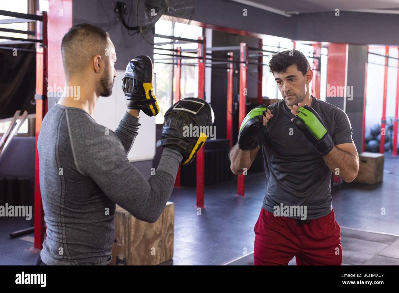Trainer mit Focus-Handschuhen und indischer männlicher Sportler, der im Fitnessstudio Punches übt, Kopierraum Stockfoto