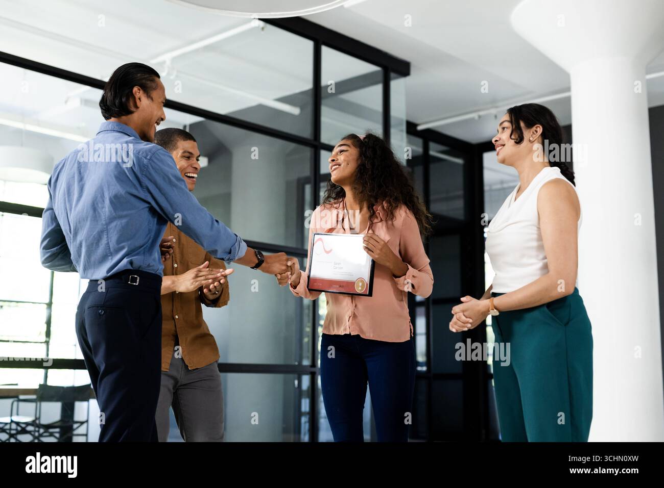 Vielseitiges Geschäftsteam feiert die Auszeichnung des Kollegen in modernen Büros Stockfoto