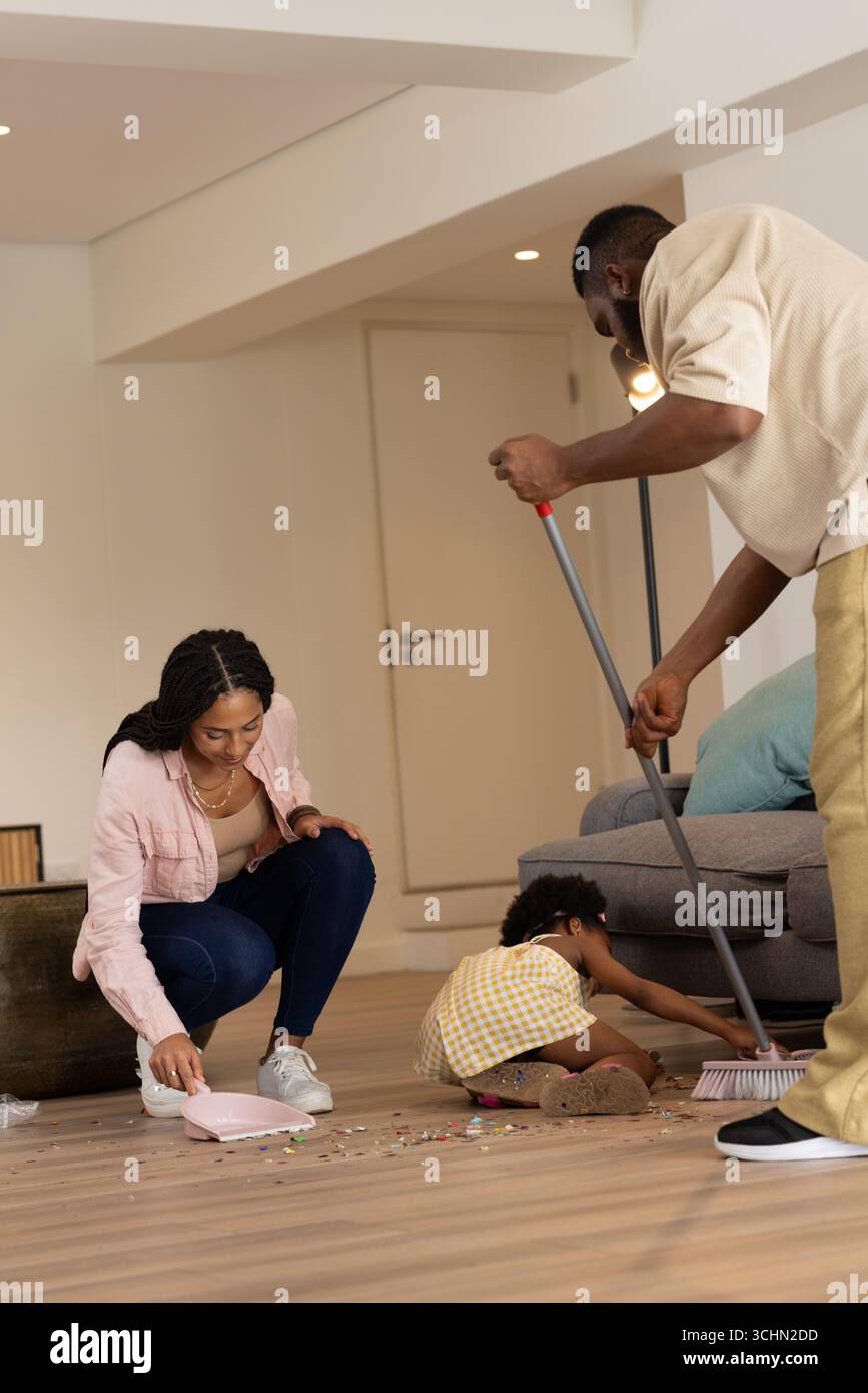 Das Wohnzimmer wird gereinigt, die afroamerikanische Familie fegt, während das Kind Eltern hilft Stockfoto