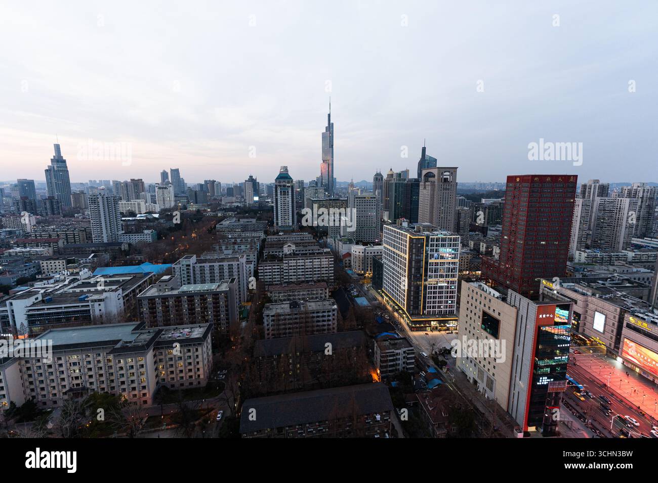Blick aus der Vogelperspektive auf eine dichte Skyline der Stadt in der Abenddämmerung mit einem hochaufragenden Wolkenkratzer, modernen Gebäuden und leuchtenden Straßen. Stockfoto