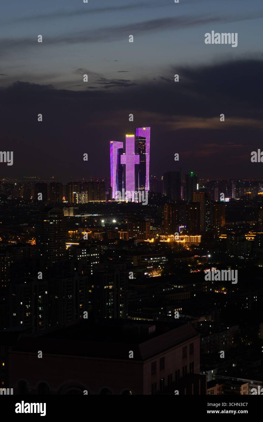 Nächtlicher Luftanblick auf eine dunkle Skyline der Stadt, hervorgehoben durch einen markanten Wolkenkratzer-Komplex, der mit leuchtenden lila LED-Lichtern leuchtet. Stockfoto