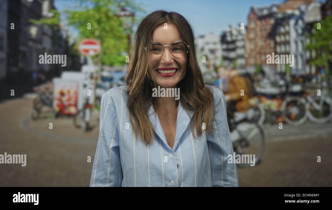 Lächelnde Frau in blauem Hemd mit Brille und breitem Grinsenfinger, der auf den sonnendurchfluteten Kanal auf der Straße zeigt; unbeschwerte Freude. Stockfoto