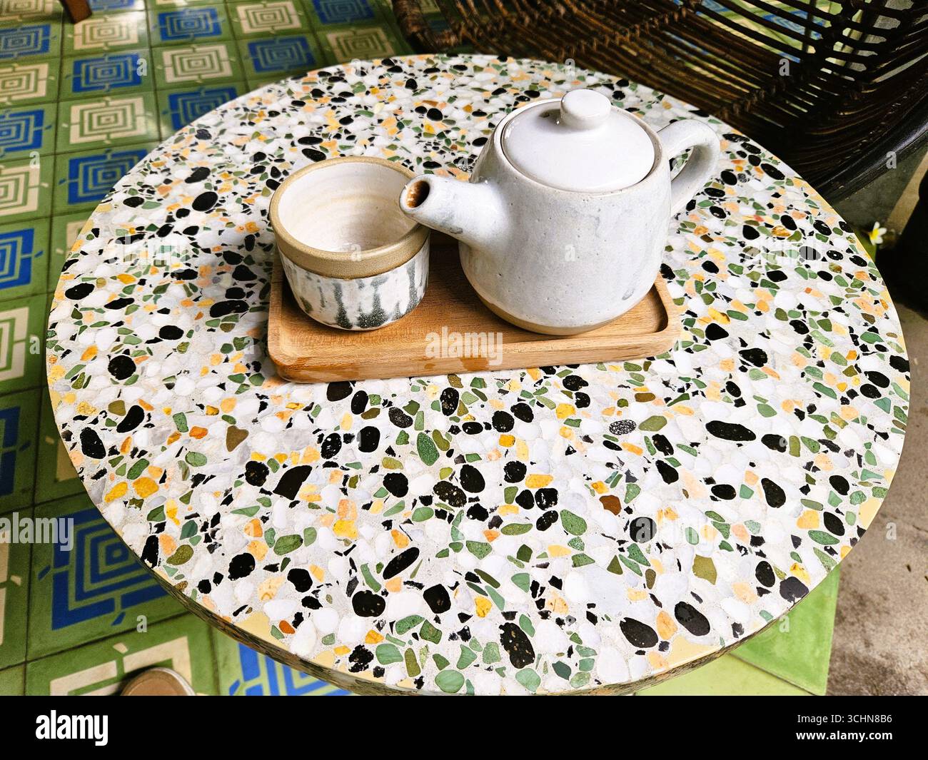 Weiße Teekanne mit Tasse auf Holztablett auf Terrazzo-Tisch, einfacher Tee bei Tageslicht. - Smartphone-aufgenommenes Stockfoto