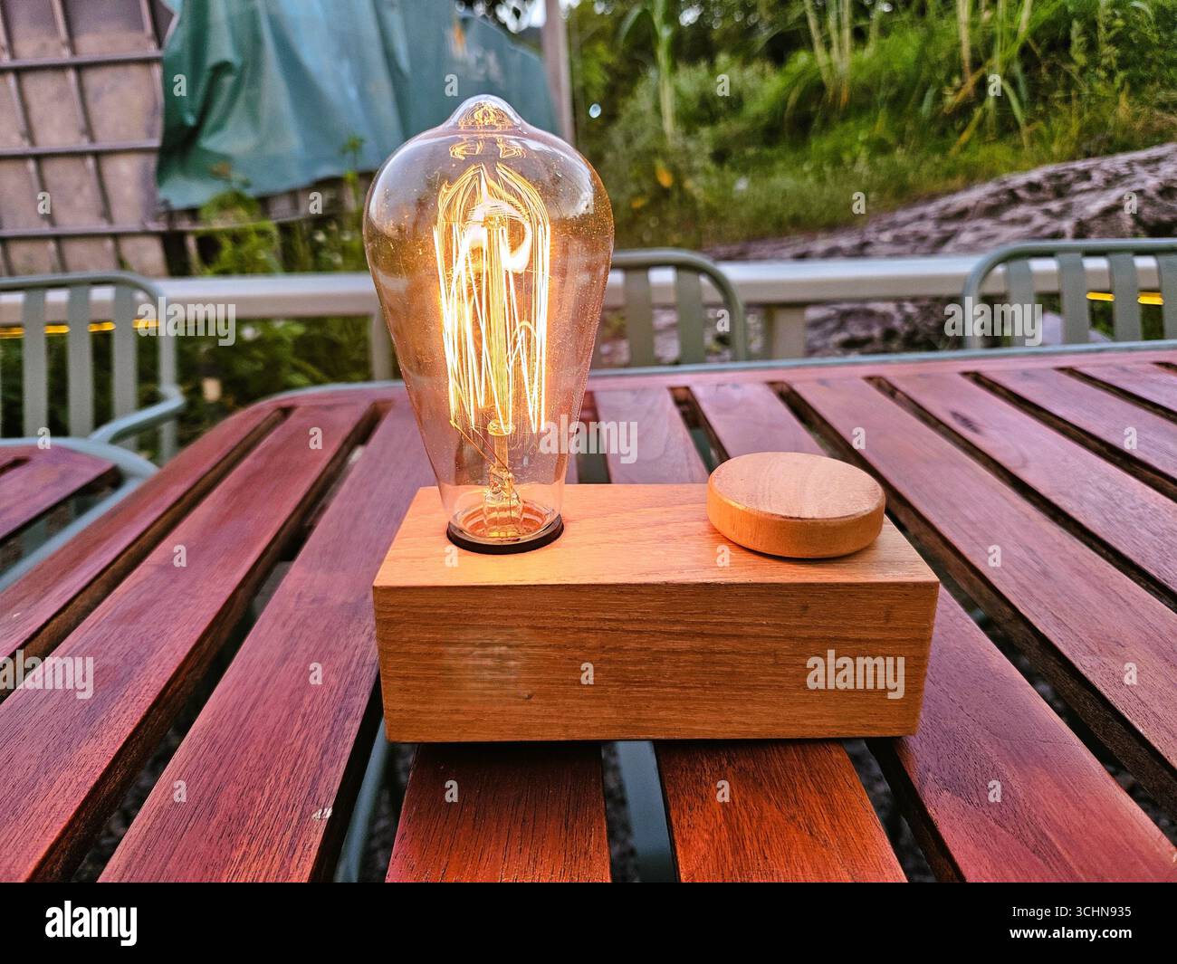 Vintage-Glühlampe mit Glühbirne auf Holztisch, warme Beleuchtung schafft gemütliche Atmosphäre - Smartphone-aufgenommenes Stockfoto