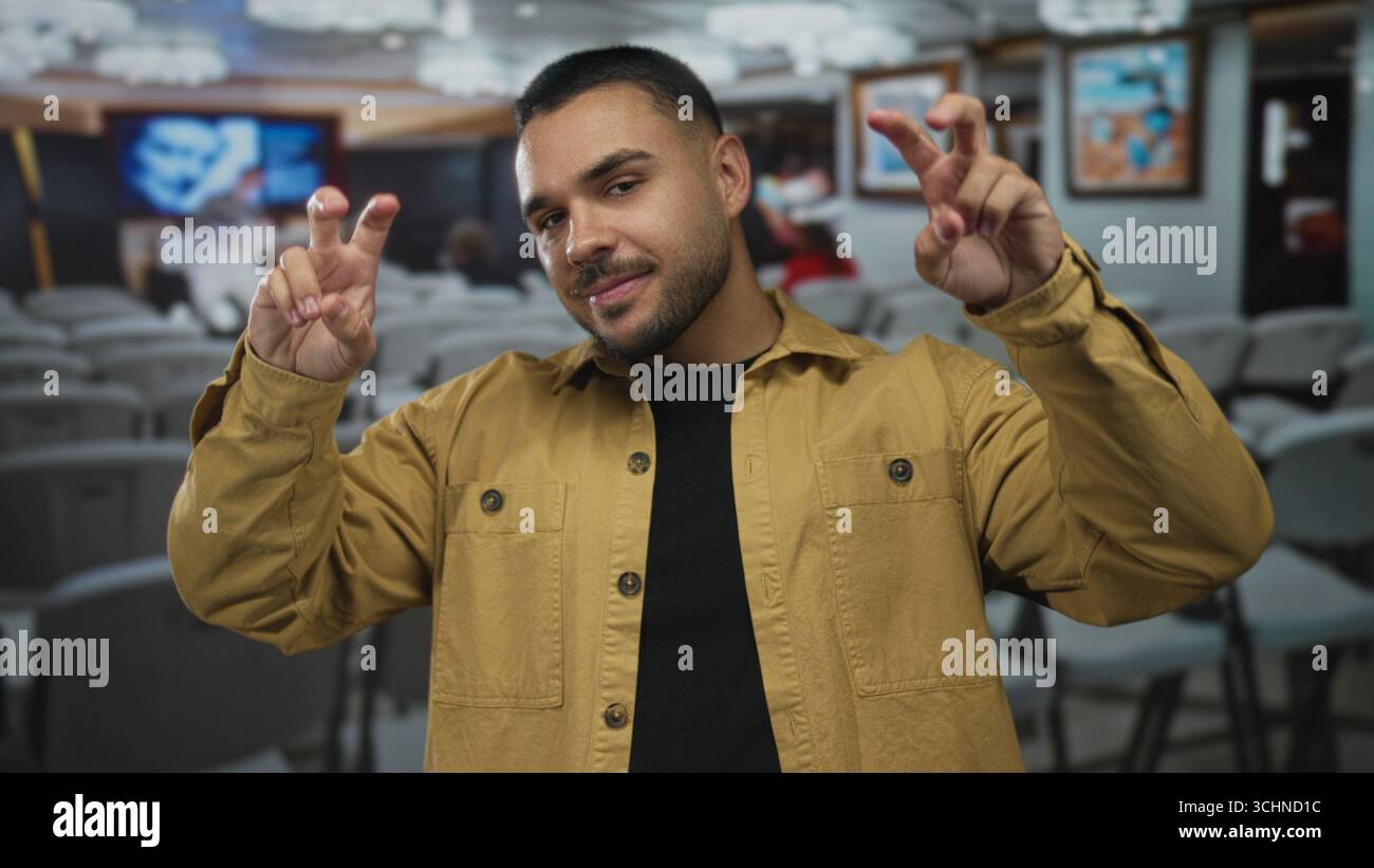 Ein Mann mit gelber Jacke hält die Finger in Luft zitiert Geste im Gebäude mit gerahmten Gemälden an den Wänden; ironischer Sarkasmus. Stockfoto