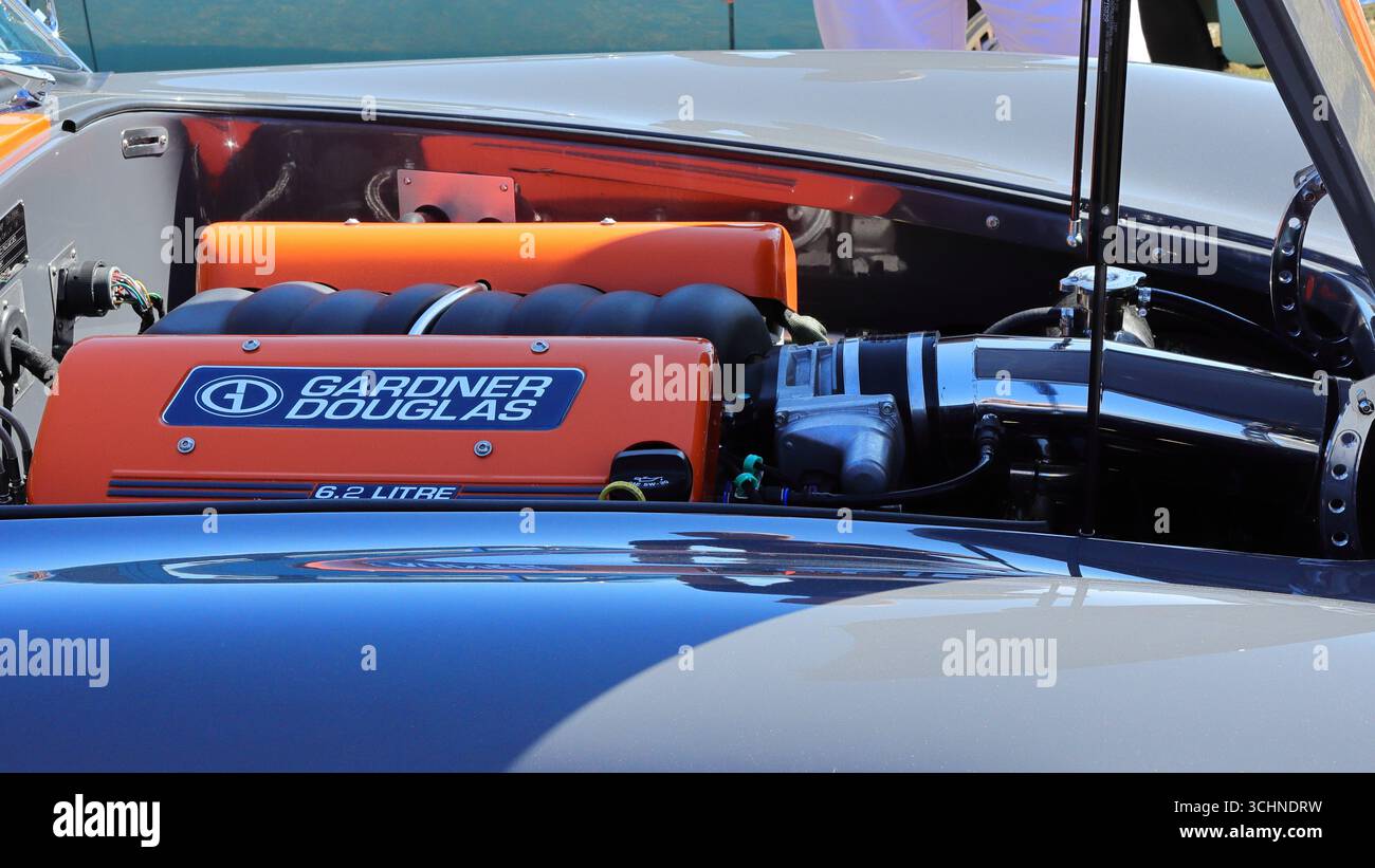 Ein Motorraum ist der Fokus dieses Nahaufnahme-Fotos. Der Motor ist in leuchtendem Orange gehalten und auf der Abdeckung mit dem Aufdruck „Gardner Douglas 6,2 Liter“. Um den Motorblock herum sind verschiedene Rohre, Schläuche und mechanische Komponenten sichtbar. Die umgebende Karosserie ist glänzend und mit blauen und weißen Reflexen versehen. Illustrativ, Editorial: Die Stokes Bay Car Rally in Gosport, Hampshire, England. 25. August 2025. Stockfoto