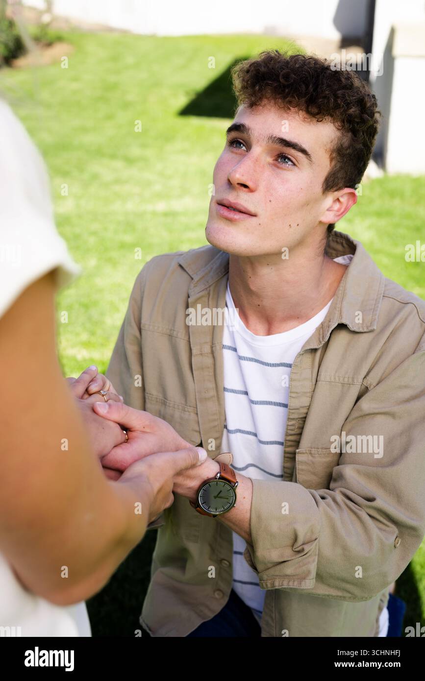 Junger Mann, der draußen einen Antrag macht, Hände hält, hoffnungsvoll und emotional aussieht Stockfoto