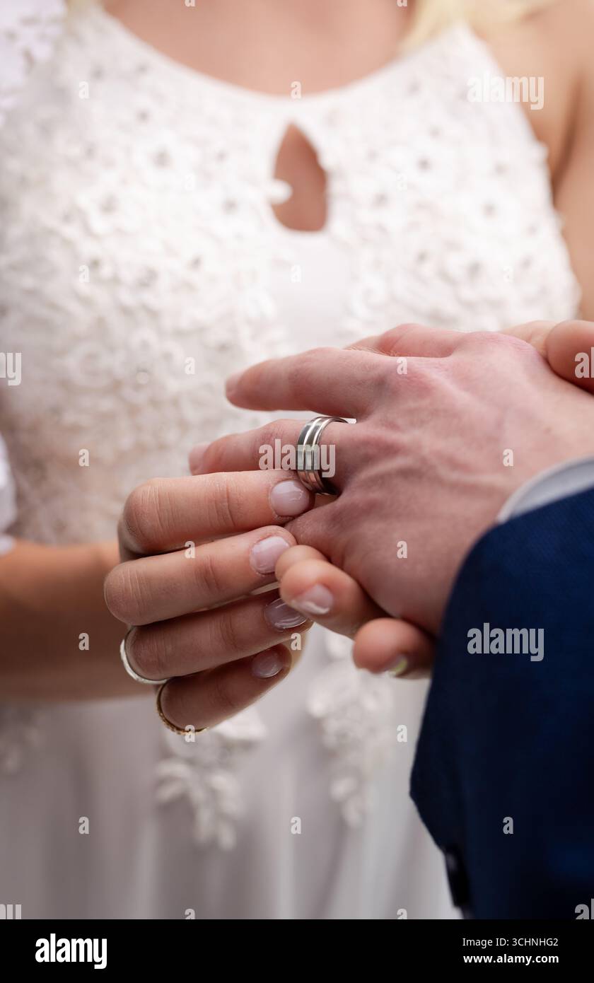 Braut, die während der Hochzeitszeremonie einen Ring am Finger des Bräutigams legt, symbolisiert die Liebe Stockfoto