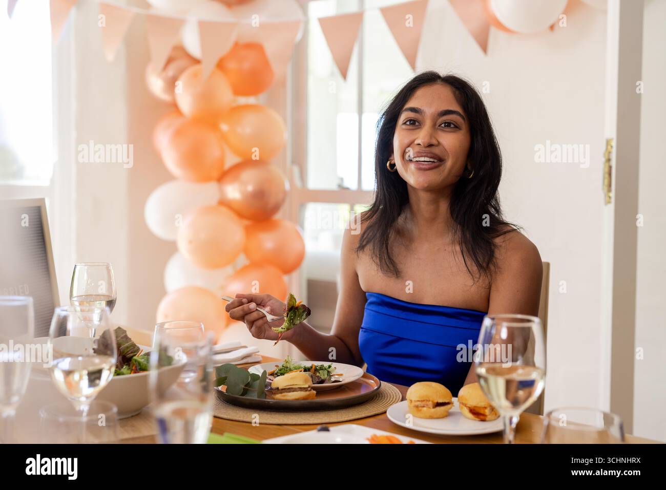 Lächelnde Frau in blauem Kleid, die bei festlicher Hochzeitsfeier das Essen genießt Stockfoto