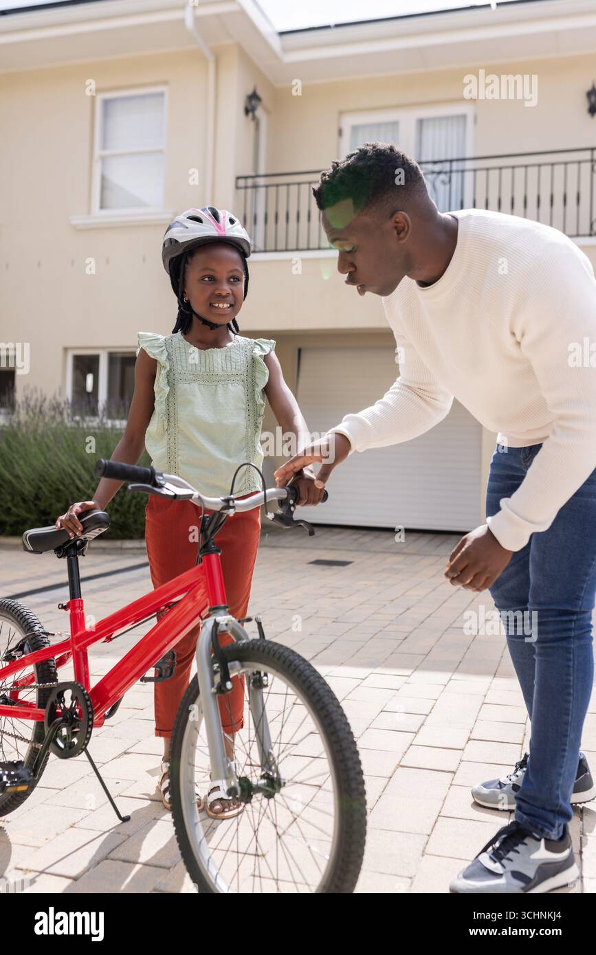 Vater bringt Tochter bei, Fahrrad in der Einfahrt zu fahren, beide lächeln glücklich Stockfoto