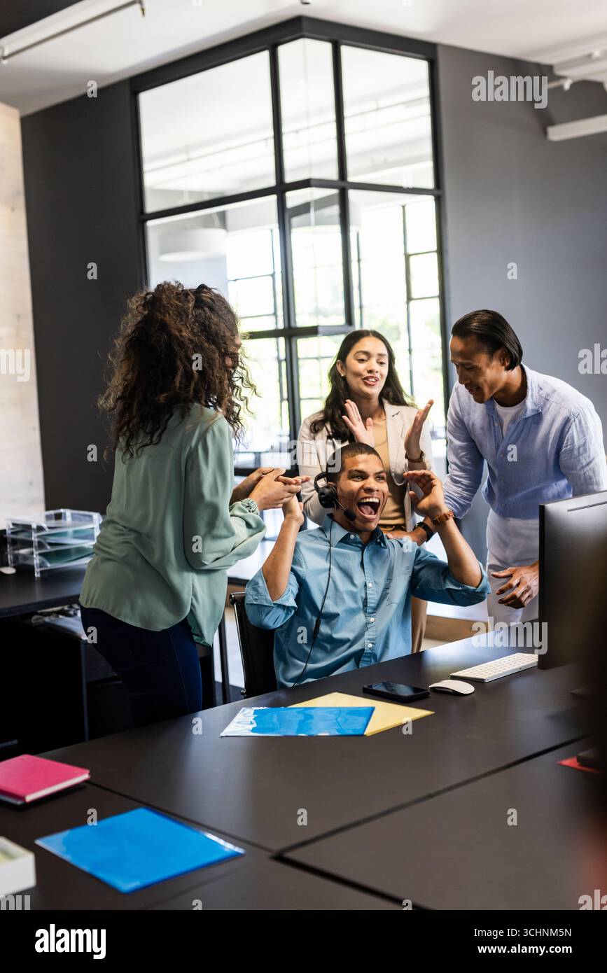 Team feiert Erfolg im modernen Büro, Mann mit Kopfhörern jubelt Stockfoto