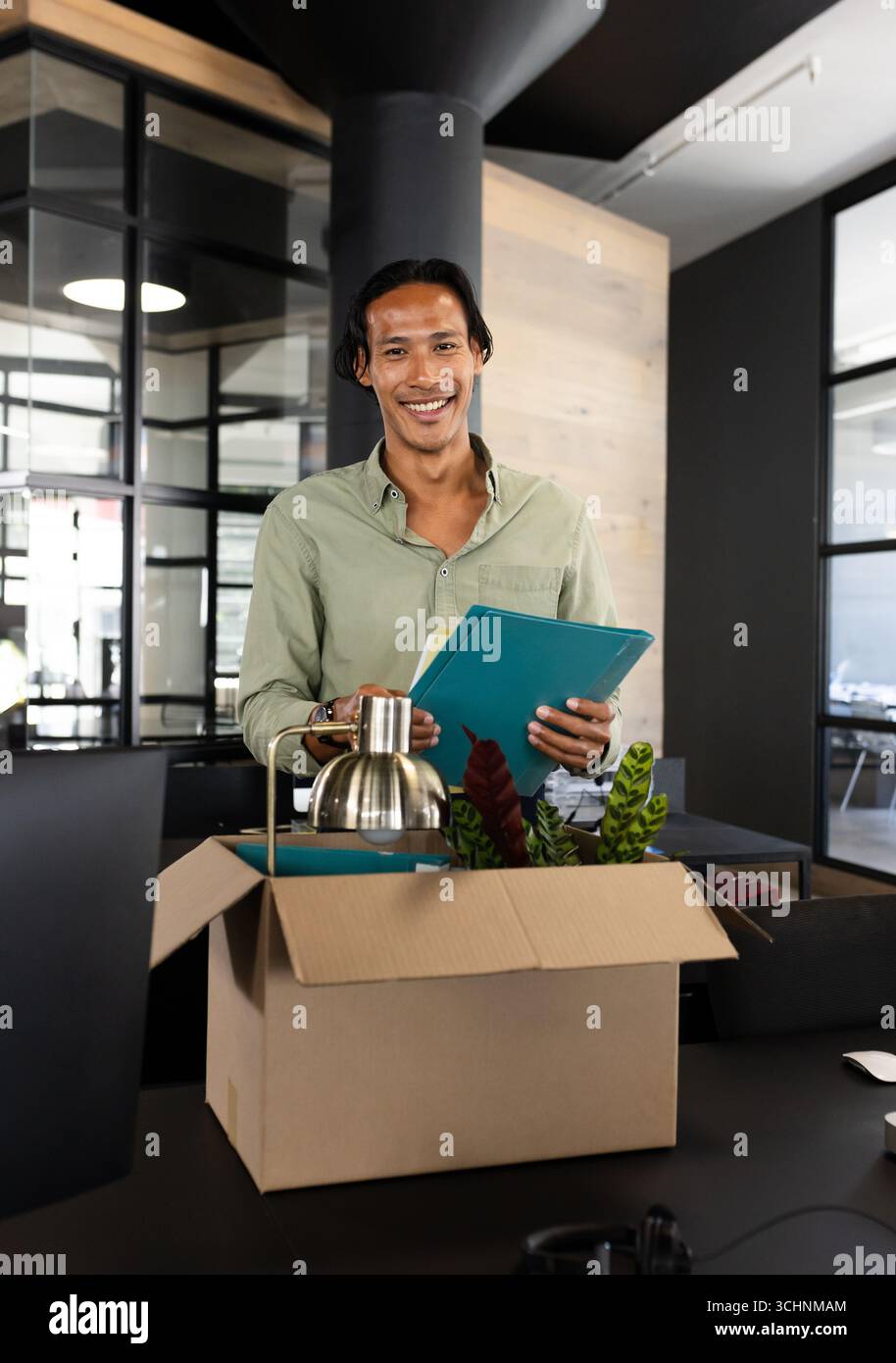 Ein lächelnder Mann, der Bürobedarf aus der Kiste in einem modernen Arbeitsbereich auspackt Stockfoto