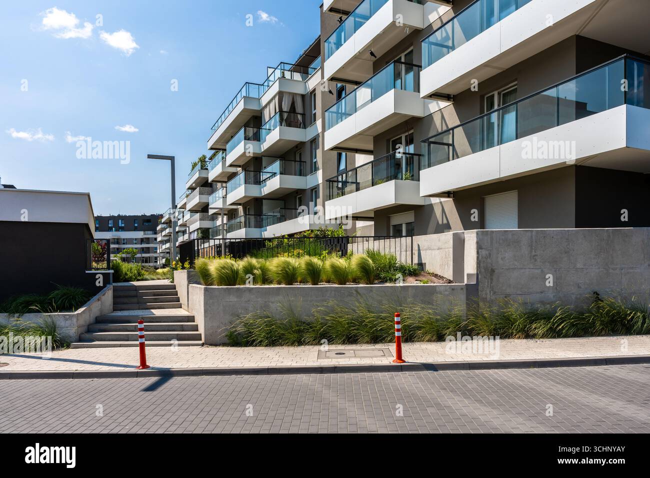 Moderne weiße Apartmentfassade mit Balkonen und begrüntem Grün im Vordergrund Stockfoto