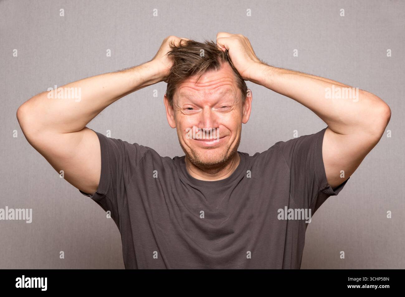 Sehr frustrierter Mann mit Gesichtsausdrücken, der Haare auf einem Studio-Foto mit grauem Hintergrund zieht, frustrierter europäischer Mann mittleren Alters, Kopierraum Stockfoto