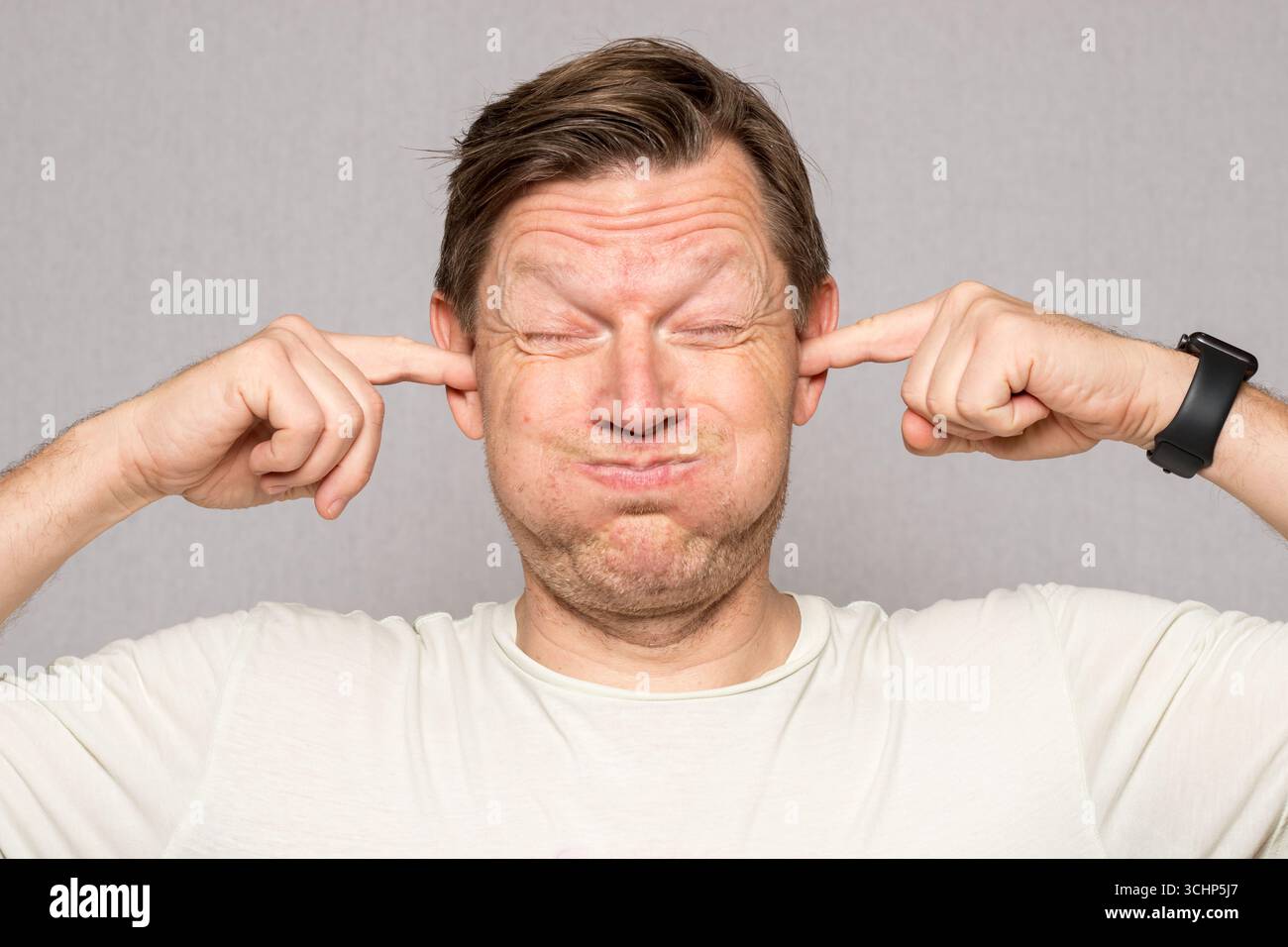 Mann mit Fingern in den Ohren, die Augen schließen und frustriertes Gesicht, kein Tonbild, geistige Gesundheit Mann, Atelier-Bild des Mannes mit Gesichtsausdruck Stockfoto