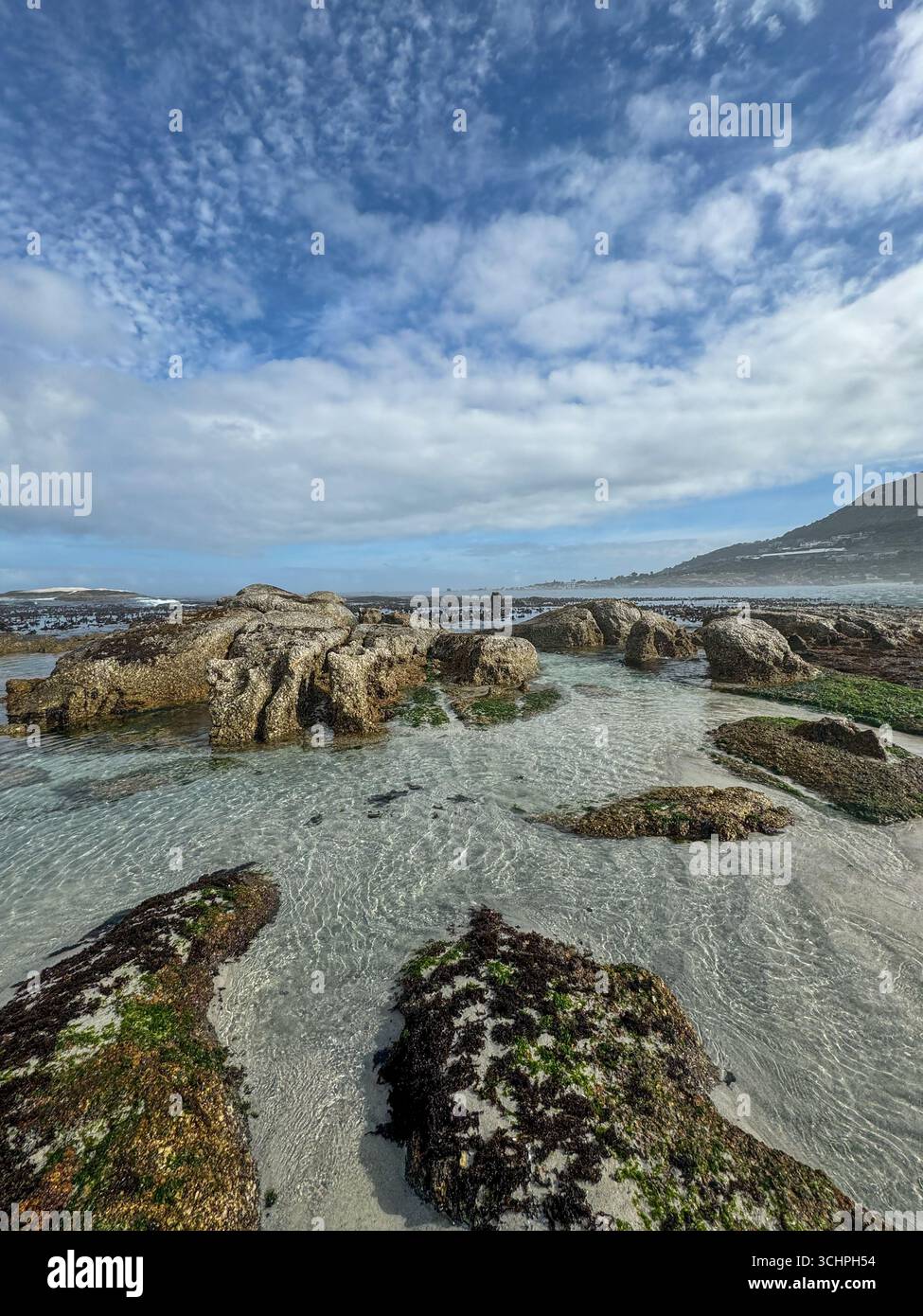 Eine Weitwinkelaufnahme eines felsigen Strandes in Kapstadt. Das Foto zeigt das unberührte, klare Wasser, das über den Sand und die Felsen im fließt - Smartphone-aufgenommenes Stockfoto