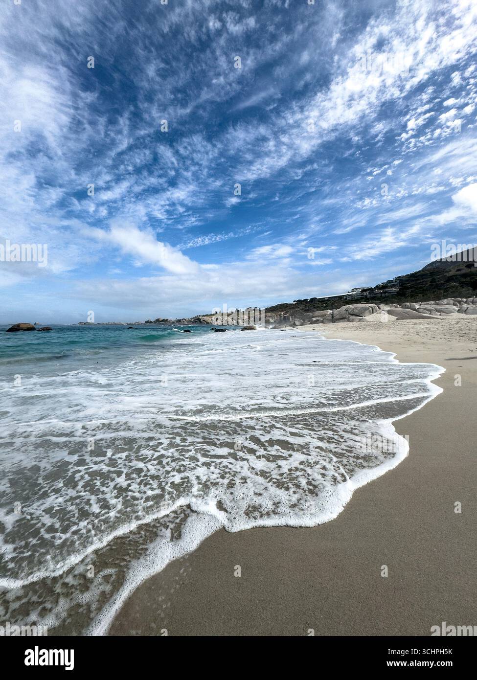 Eine Weitwinkelaufnahme eines felsigen Strandes in Kapstadt. Das Foto zeigt das unberührte, klare Wasser, das über den Sand und die Felsen im fließt - Smartphone-aufgenommenes Stockfoto