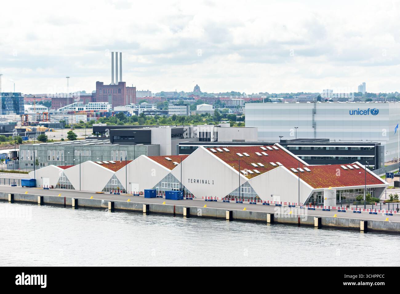 UNICEF Global Supply Hub Christianshavn Denmark // CHRISTIANSHAVN, Denmark — Terminal 1, ein modernes Gebäude mit einem markanten roten, begrünten Dach, ist im Vordergrund zu sehen, im Hintergrund neben dem UNICEF Supply Warehouse Building. In diesem globalen UNICEF-Versorgungszentrum in Kopenhagen, Dänemark, befindet sich ein über 20.000 Quadratmeter (215.000 Quadratfuß) großes Lager und ist damit das größte halbautomatische Lager für humanitäre Hilfe weltweit. Die Einrichtung, eine Spende der dänischen Regierung, kann bis zu 36.000 Paletten mit Vorräten lagern. Lagerhaltung und Vertrieb sind die Schlüsselfaktoren Stockfoto