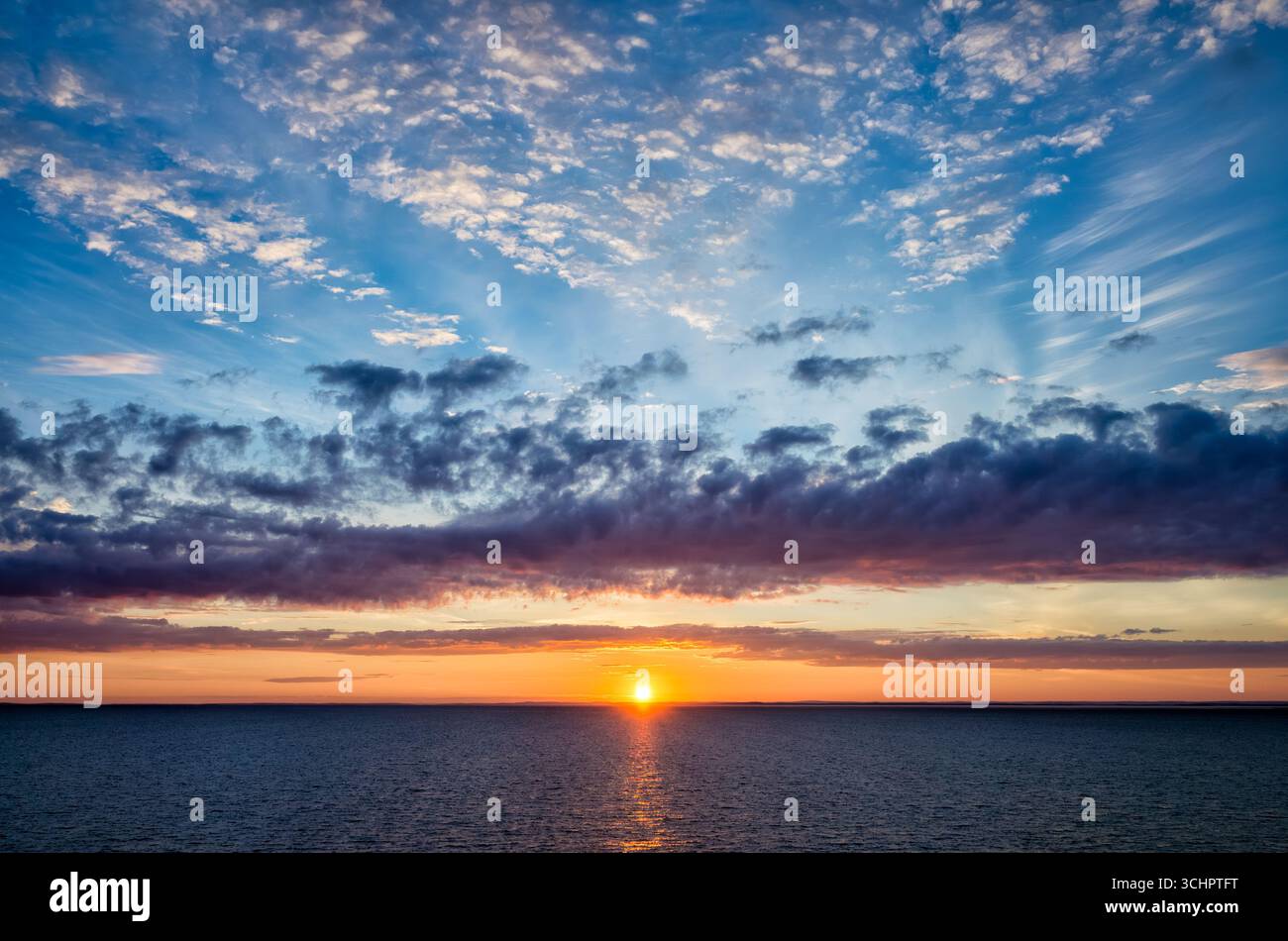 Sonnenaufgang über der schwedischen Küste von Kopenhagen nach Oslo Fähre Strömstad Schweden // STRÖMSTAD, Schweden — Ein lebendiger Sonnenaufgang erleuchtet den Himmel über den Gewässern vor der schwedischen Küste in der Nähe von Strömstad. Die Szene fängt den Übergang von Nacht zu Tag ein, während die Sonne gerade über den Horizont steigt und ein warmes Licht über das Meer wirft. Wolken verstreut sich über die blaue Fläche, einige von Orange- und Violetttönen der aufgehenden Sonne. Diese Aussicht ist charakteristisch für die Küstenlandschaft in der Region Västra Götaland in Schweden. Stockfoto