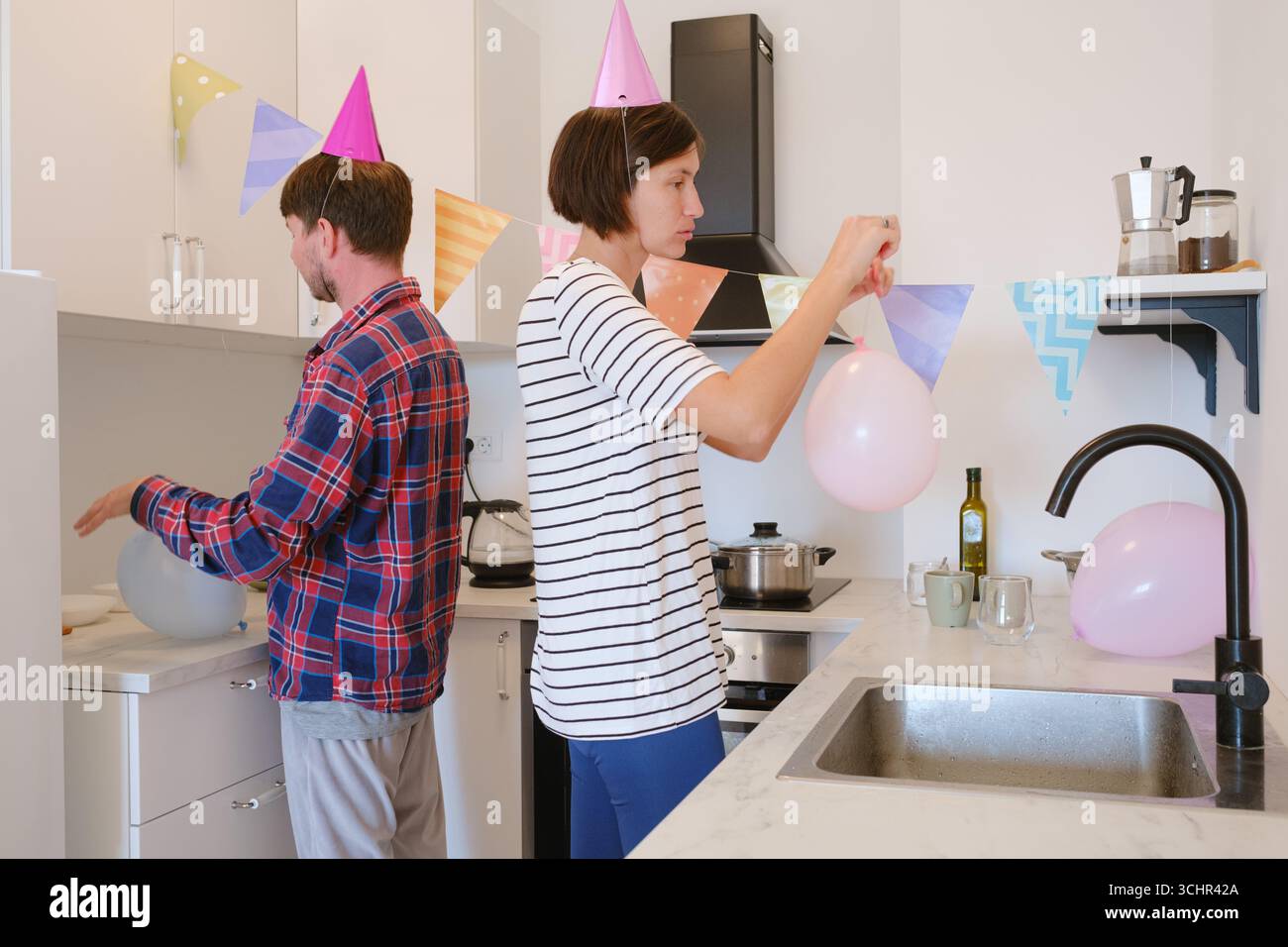 Das junge Paar feiert zu Hause gemütlich Geburtstag und genießt Kuchen und Lachen in warmer Atmosphäre. Fröhliche Atmosphäre, farbenfrohe Dekoration und gemeinsames Lächeln. Vorbereitung auf den Feiertag, Dekoration des Zimmers Stockfoto