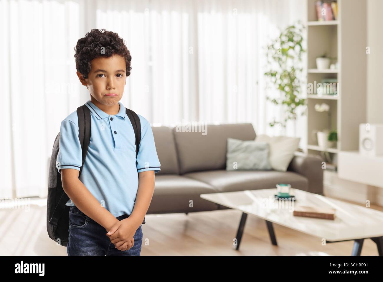 Ernster kleiner Junge mit Rucksack, der zu Hause im Wohnzimmer steht Stockfoto