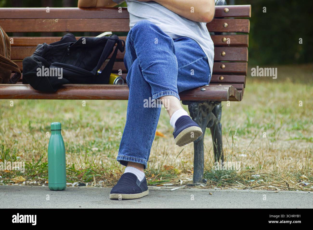 Digitaler Nomad macht produktive Pause: Remote-Mitarbeiter mit Rucksack und wiederverwendbarer Stahlflasche auf einer Bank im Park. Work-Life-Balance-Konzept Stockfoto