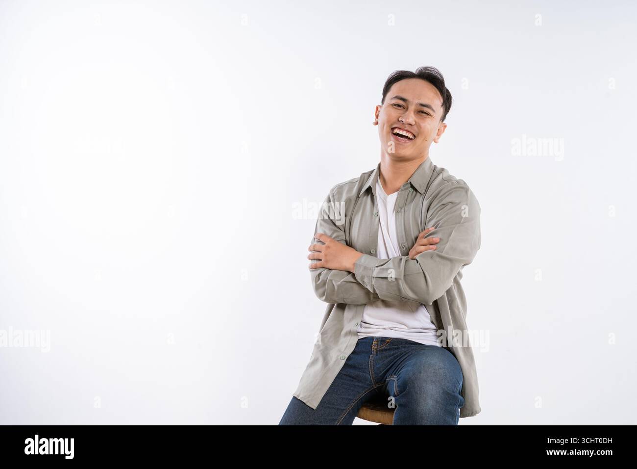 Ein glücklicher junger Mann, der auf einem Hocker-Studio-Porträt voller Leben und Freude sitzt Stockfoto