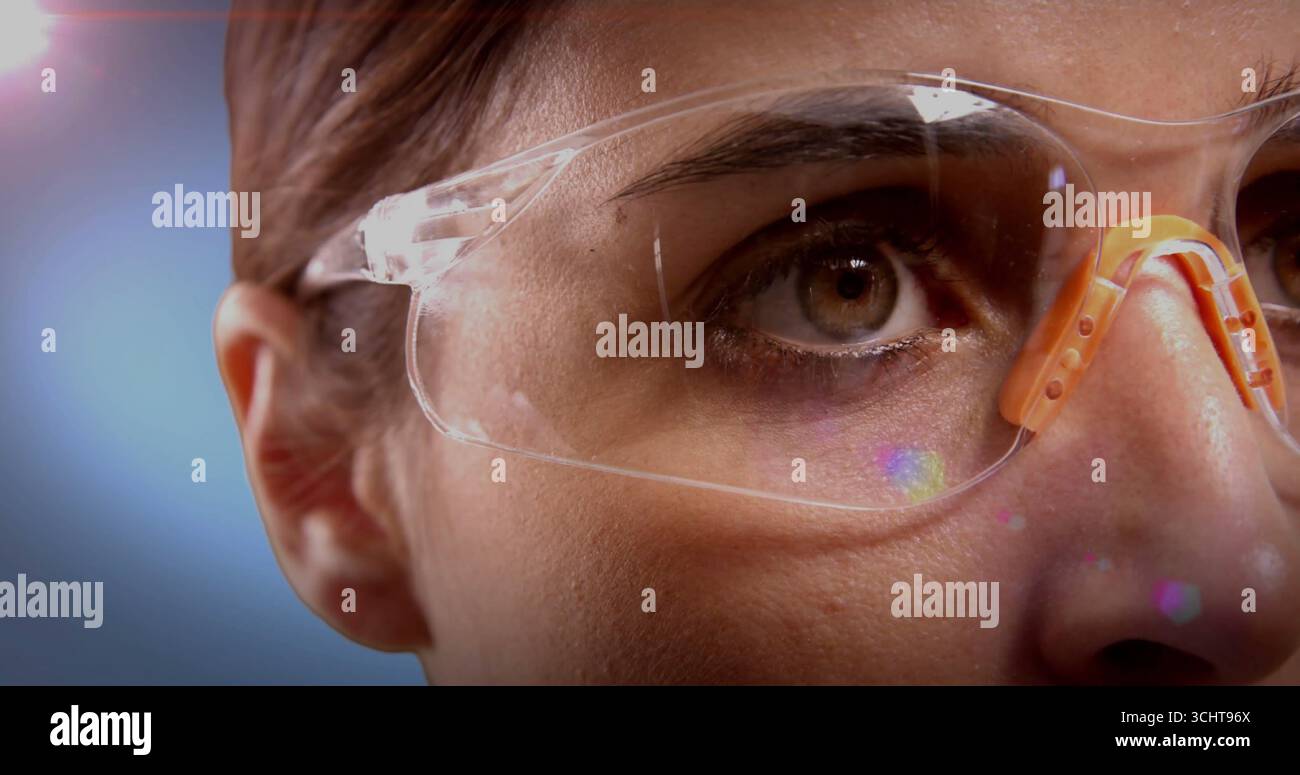 Erwachsene Frau, die im Labor eine Schutzbrille inspiziert, mit orangefarbenem Nasenpolster, das farbige Fackeln reflektiert Stockfoto