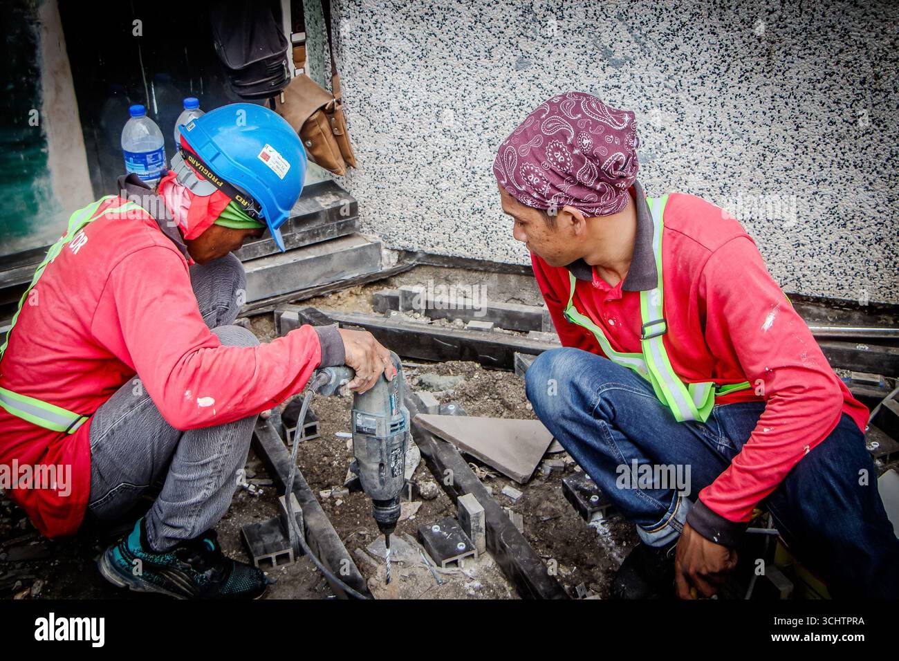 Zwei malaysische Bauarbeiter, die auf der Baustelle mit Sicherheitsausrüstung und Helmen Beton in der kuala lumpur Street malaysia zerbrechen Stockfoto