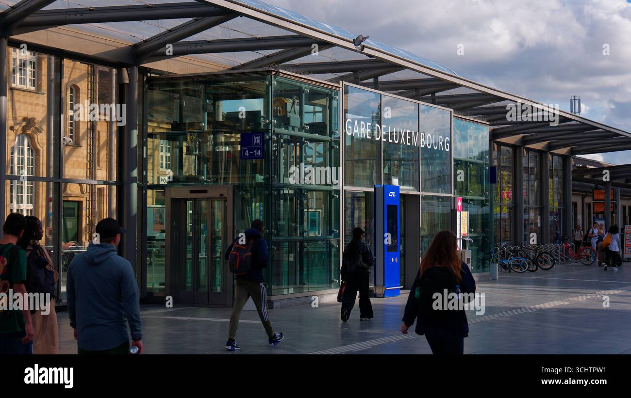 LUXEMBURG, EUROPA - 1. SEPTEMBER 2025 - Touristen, die in der Nähe des modernen Eingangs aus Glas und Stahl des Bahnhofs Gare de Luxembourg spazieren gehen Stockfoto