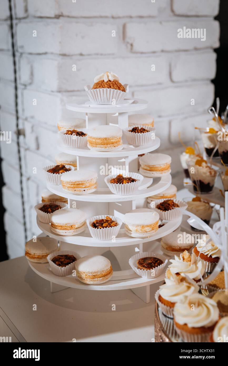 Luxuriöse Schokoriegel mit Cupcakes, Macarons und Desserts auf eleganten goldenen Tabletts Stockfoto