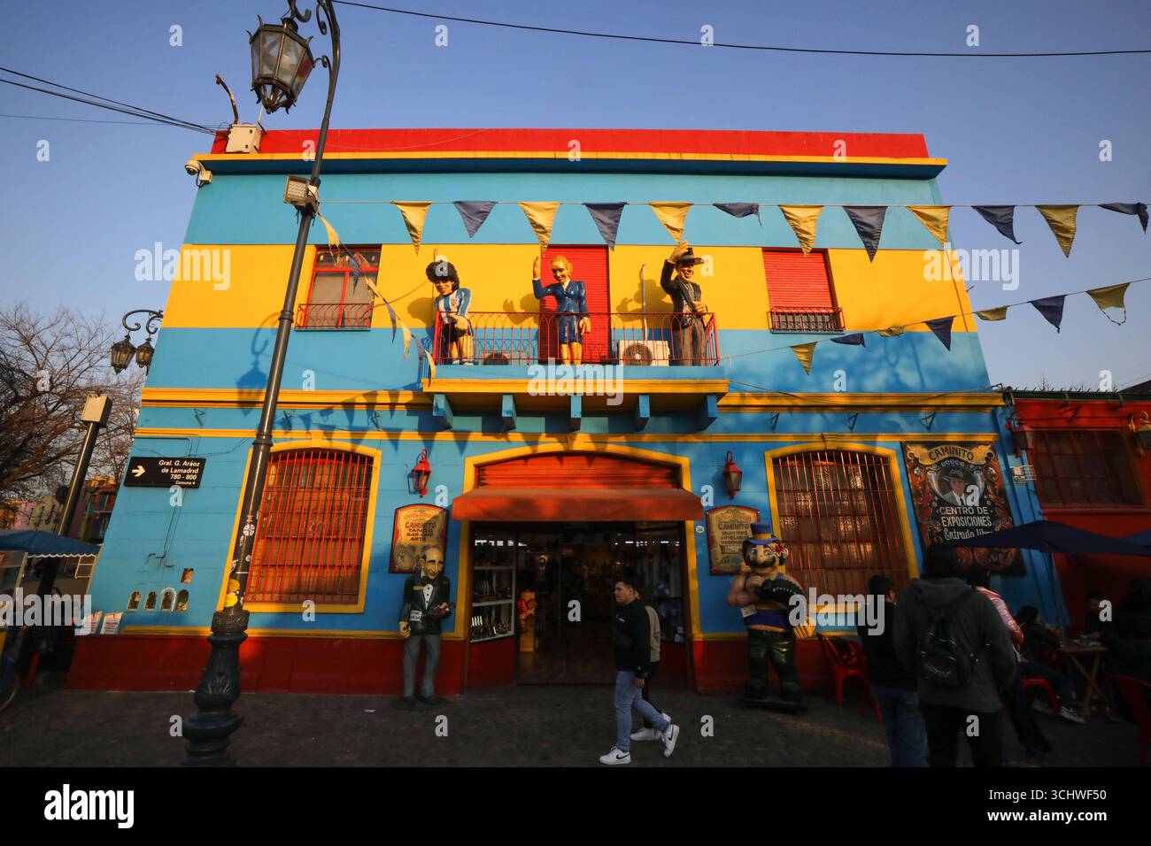 Tourismus in Argentinien die Menschen gehen an einem farbenfrohen Haus vorbei, in dem der berühmte argentinische Fußballspieler Diego Armando Maradona L, die ehemalige First Lady von Argentinien Evita Peron C, und der argentinische Sänger, Songwriter und Schauspieler und die prominenteste Figur des Tangos Carlos Gardel auf dem oberen Balkon im Stadtteil La Boca in Buenos Aires, Argentinien, 21. Juli 2025, dargestellt sind. La Boca ist ein historisches Arbeiterviertel in Buenos Aires. Der Name Boca bedeutet Mündung im Englischen und bezieht sich auf seine Lage an der Mündung des Flusses. La Boca ist berühmt für seine farbenfrohen Häuser und die lebhafte Caminito Straße. Stockfoto