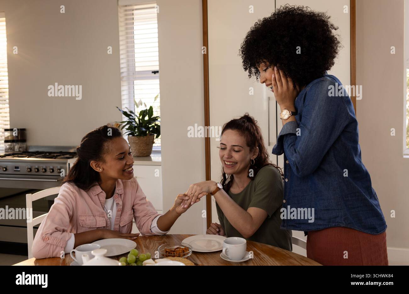Verschiedene Freundinnen feiern die Verlobung zu Hause, bestaunen Ringe und teilen freudige Momente Stockfoto