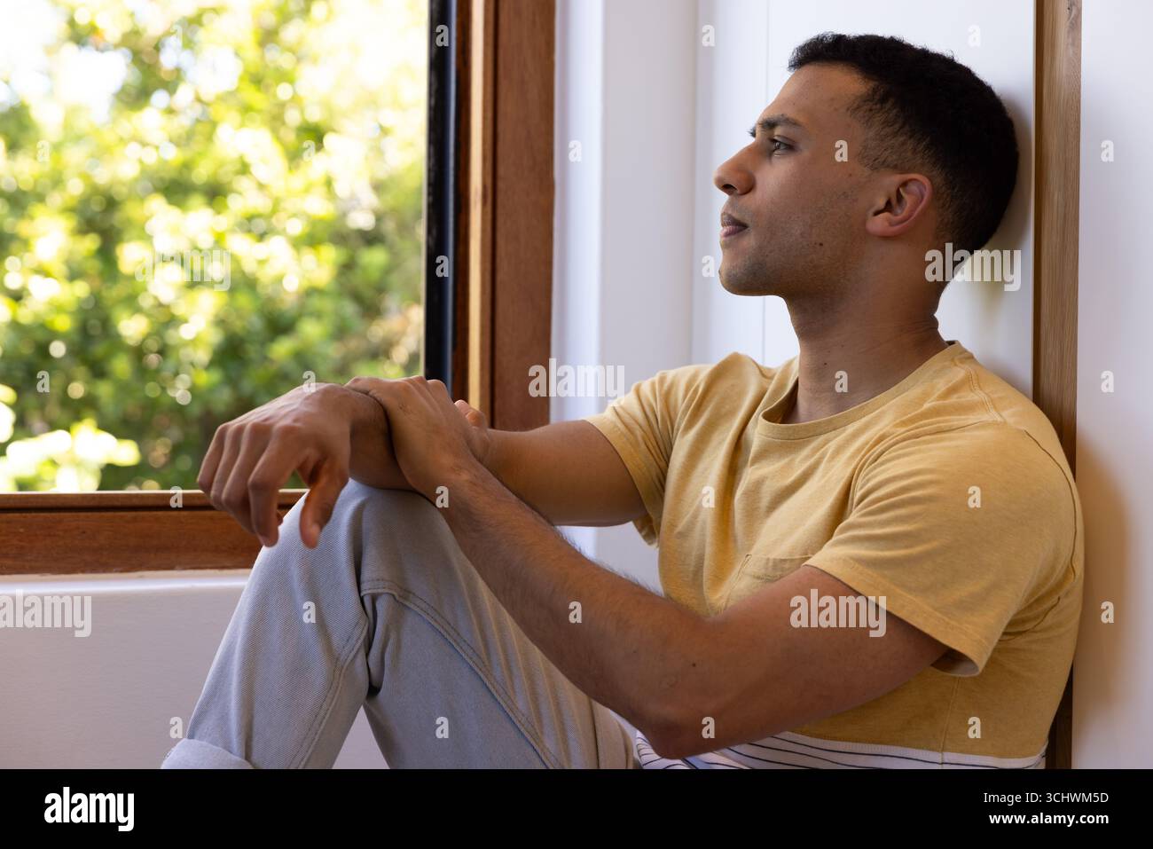 Junger Mann, der am Fenster sitzt, nach draußen blickt, in friedlichem Moment nachdenkt, zu Hause Stockfoto