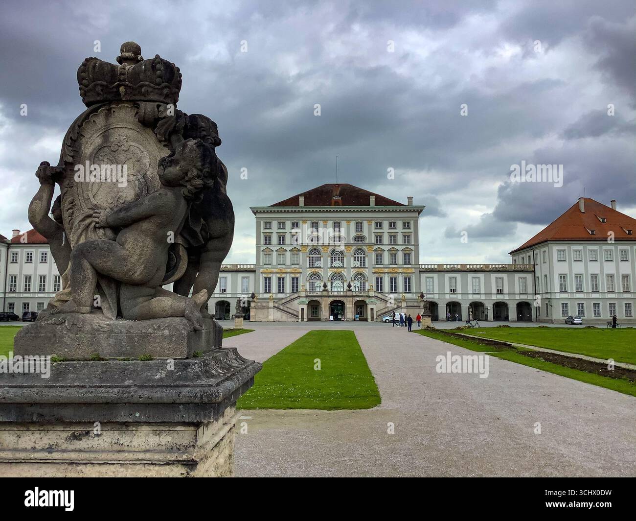 Steinskulptur vor dem Schloss Nymphenburg, München, mit königlichem Wappen und dramatischem Himmel im Hintergrund. Stockfoto