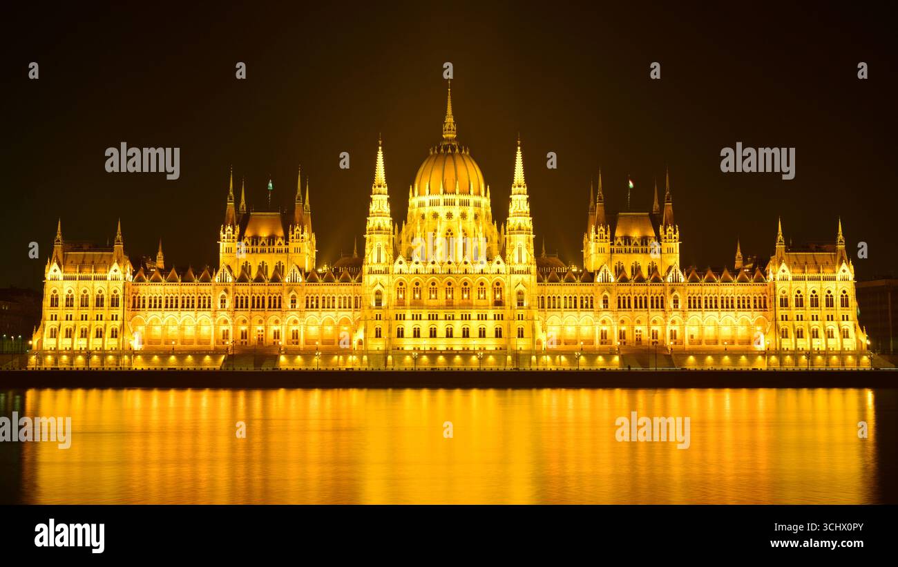 Nachtszene des riesigen ungarischen Parlamentsgebäudes in Budapest. Licht reflektiert auf der Donau. Eine sehr kalte, aber auch eine ruhige Winternacht. Stockfoto