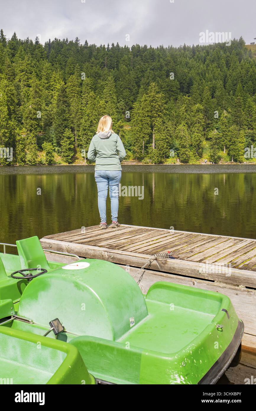 Eine Person steht auf einer Fußgängerbrücke und blickt auf einen ruhigen See im Wald, Mummelsee, Seebach, Ortenau, Schwarzwald, Deutschland Stockfoto