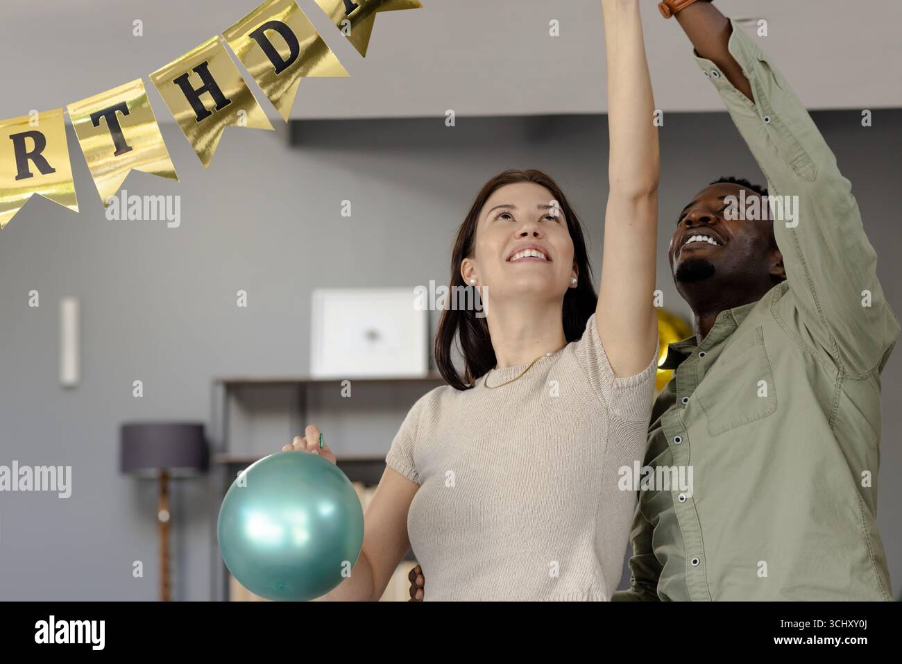 Freunde, die Geburtstagsfeiern dekorieren, Banner aufhängen und Ballon drinnen halten Stockfoto