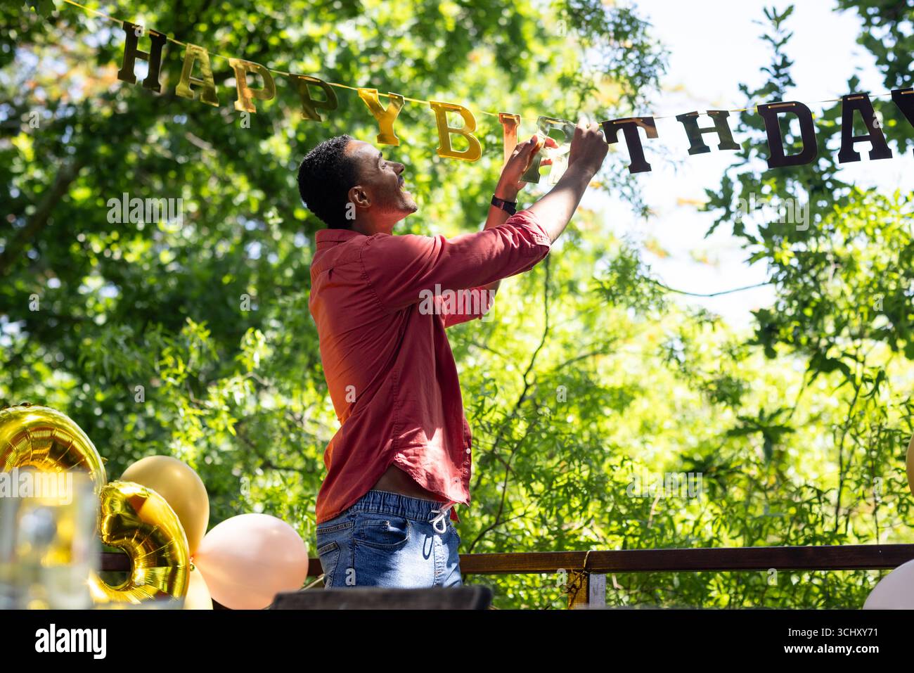 Mann, der im Garten mit Geburtstagsbanner dekoriert, sich auf die Party vorbereitet Stockfoto