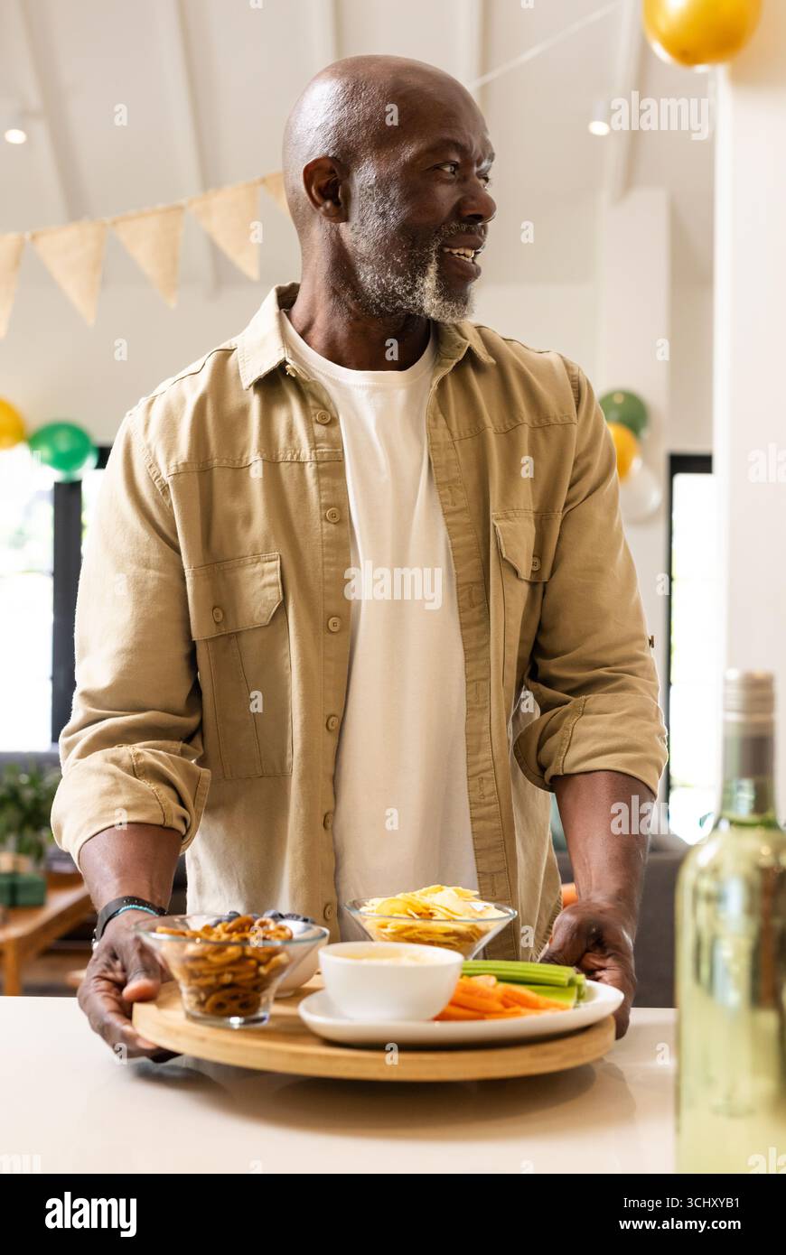 Lächelnder Mann serviert Snacks und Getränke während der festlichen Hausfeier Stockfoto
