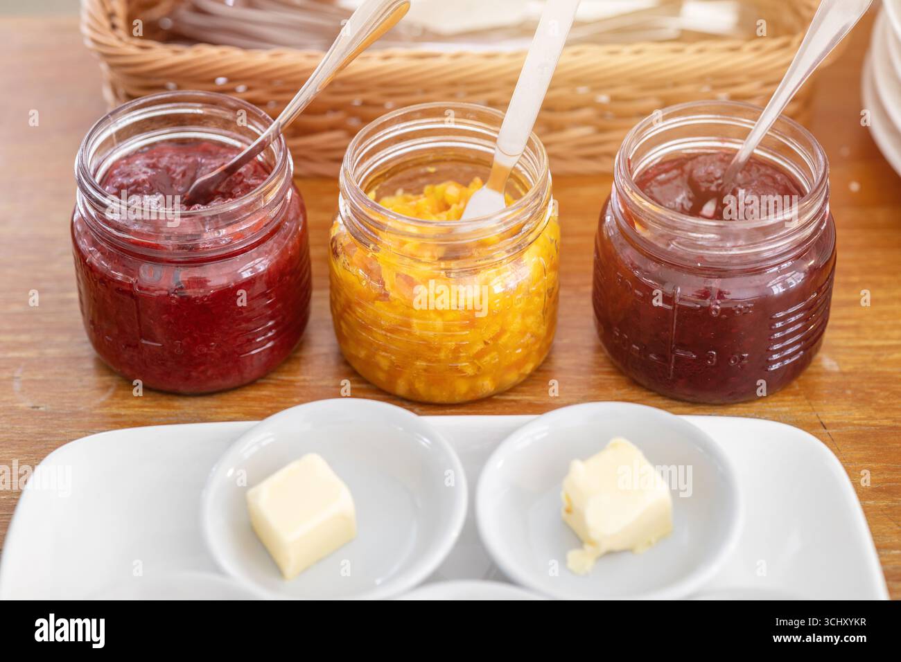 Verschiedene Geschmacksrichtungen von Obst Marmelade und frischer Butter zum Essen mit Brot Morgenmahlzeit auf dem Tisch Stockfoto