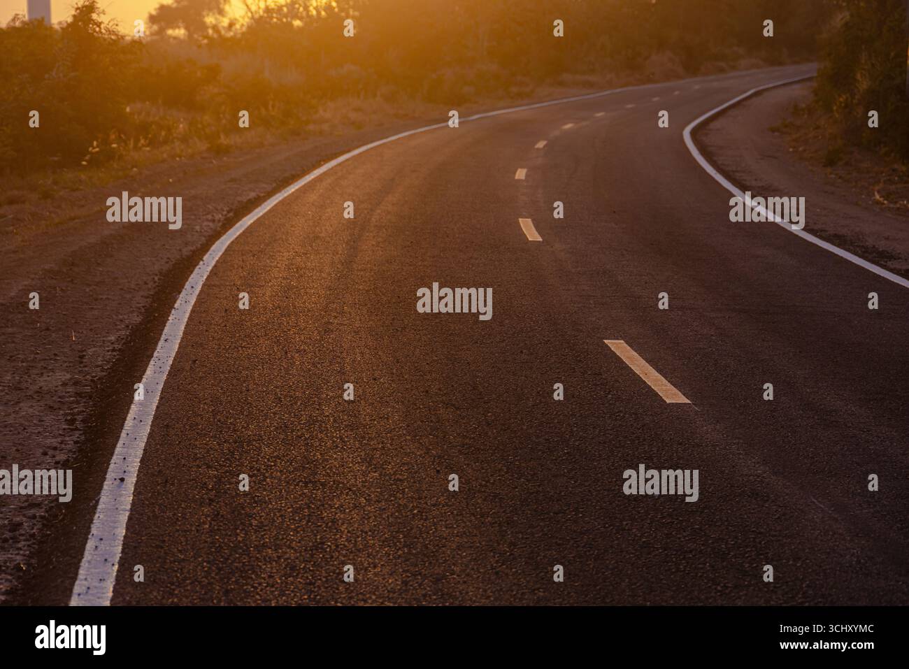 Schwarze Asphaltkurvenstraße, zweispurige Kurvenfahrt entlang des Weges vor dem Sonnenuntergang auf dem Land Stockfoto