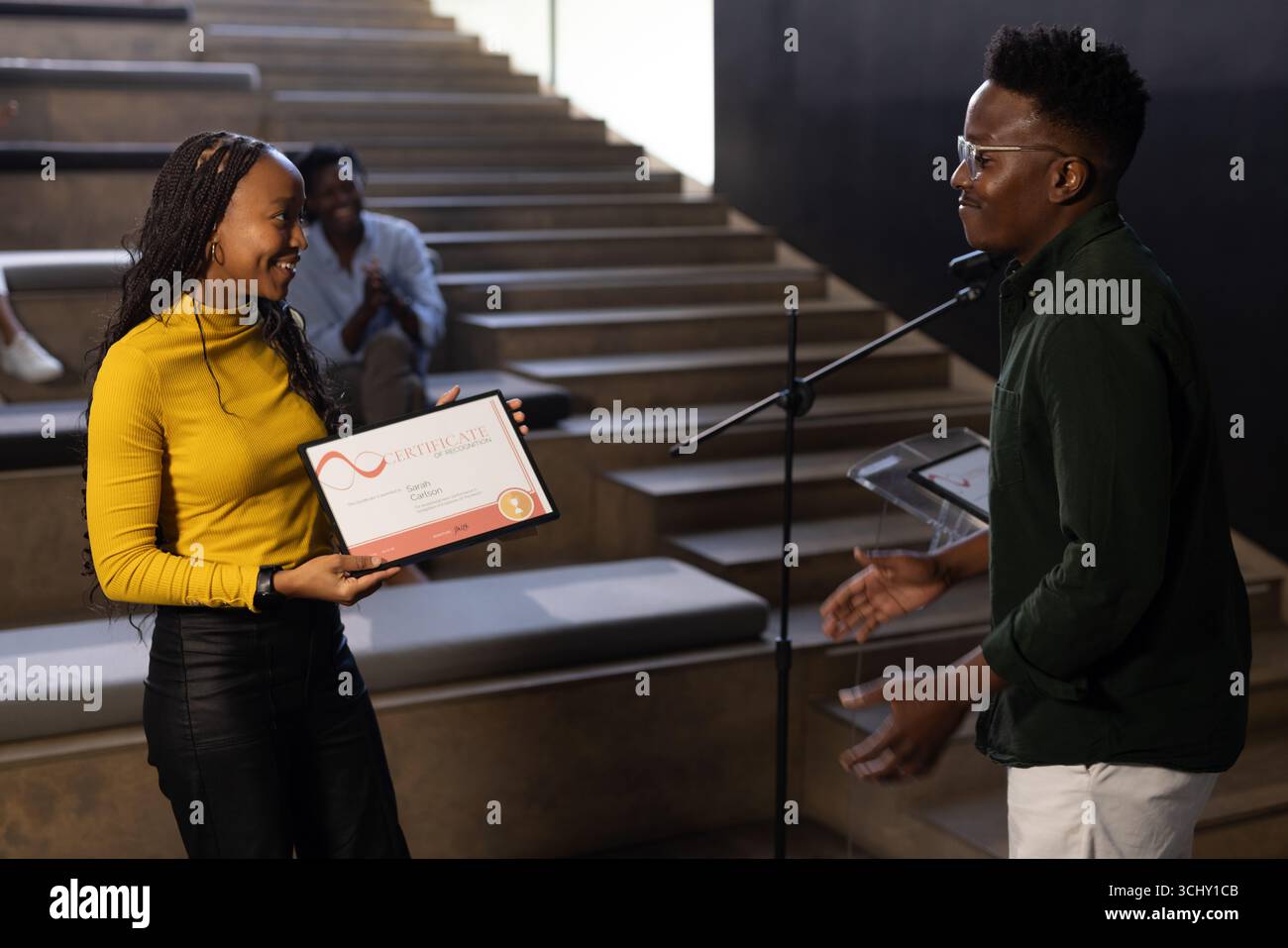 Frau, die ein Zertifikat von Mann auf der Bühne während eines Geschäftsseminars erhält Stockfoto
