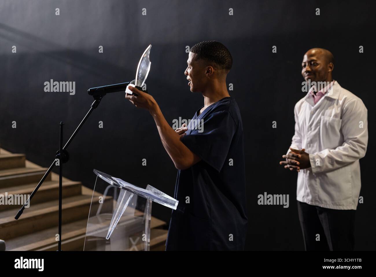 Mann, der den Preis auf der Bühne überreicht, während der Kollege mit Stolz beobachtet Stockfoto